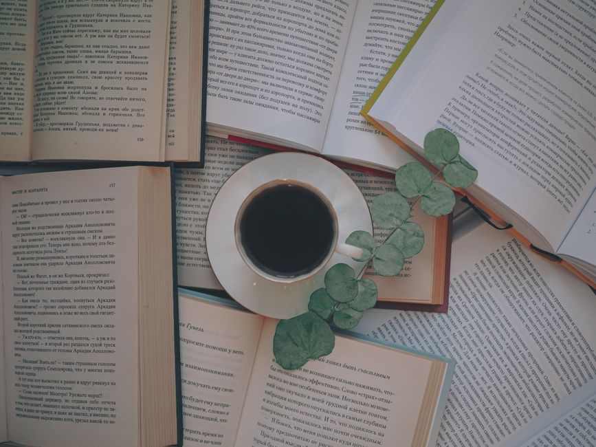 A relaxing still life with a cup of black coffee among open books and green leaves, shot from above.