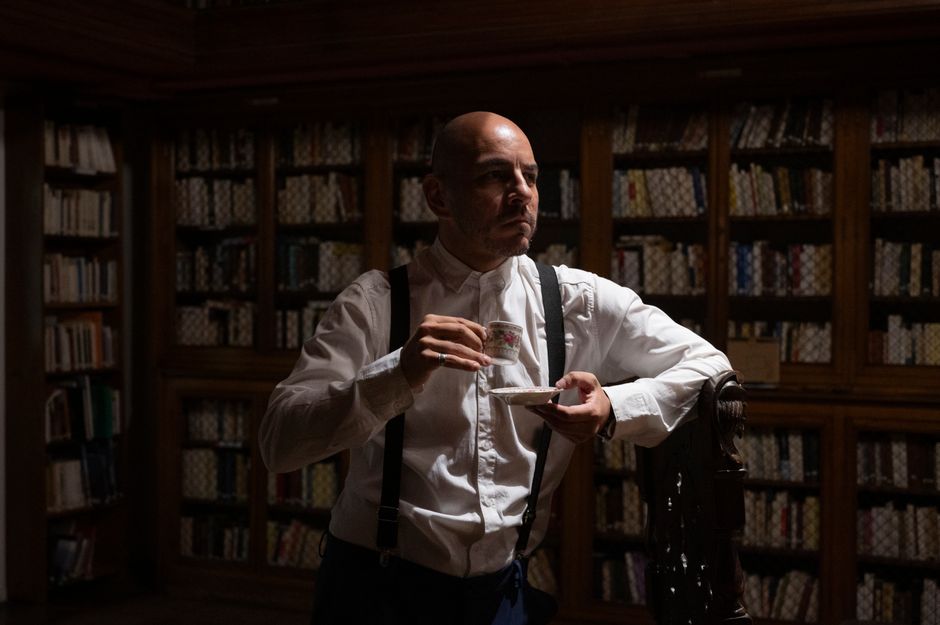 A man enjoys tea in a dimly lit vintage library, creating a classic ambiance.