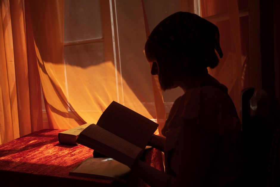Silhouette of a person reading by a dimly lit window, creating a serene atmosphere.