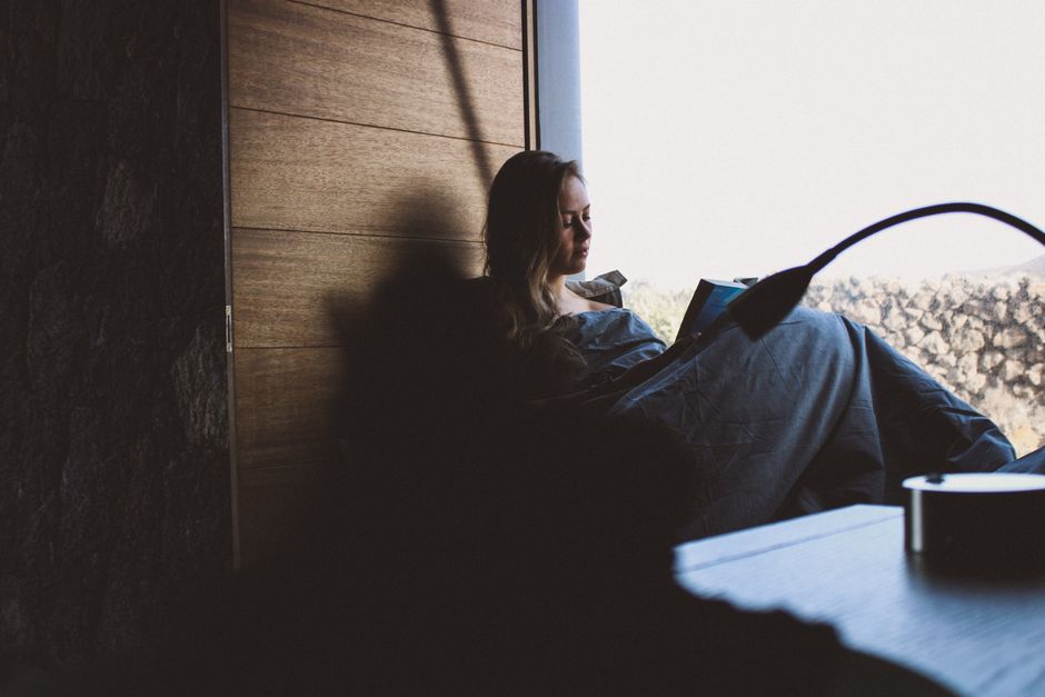Woman relaxing and reading by a window with natural light. Perfect for cozy indoor scenes.