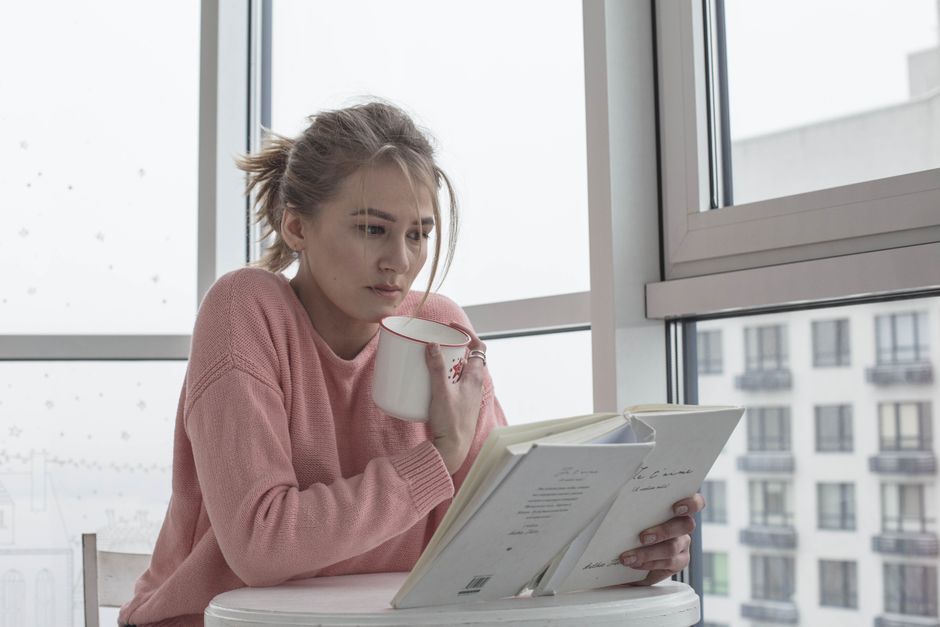 Casual woman enjoying a book with coffee by a bright window scene.