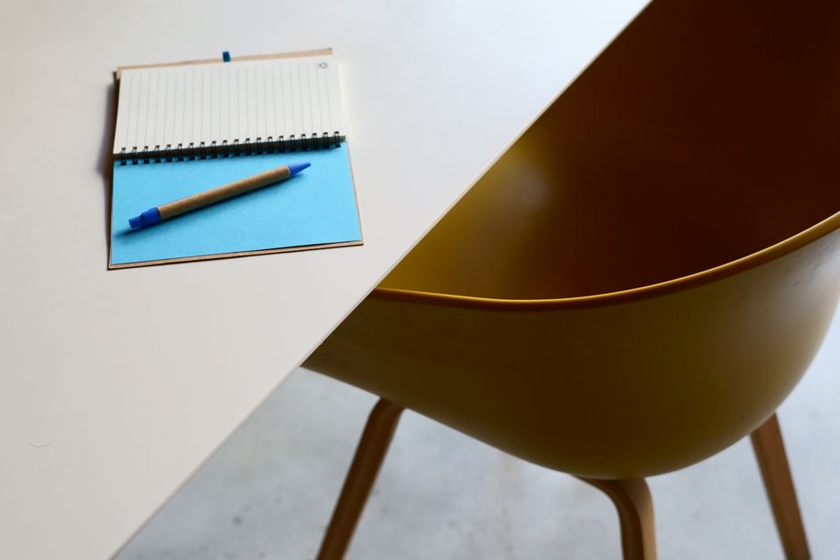 Minimalist workspace featuring a table, notebook, and modern yellow chair.
