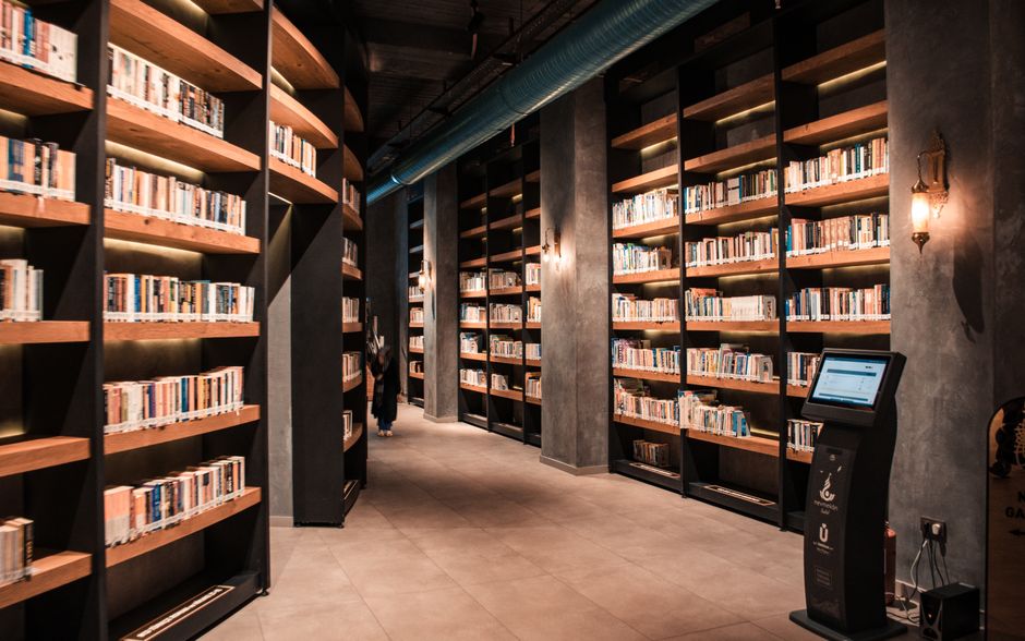 A spacious library featuring tall wooden bookshelves filled with books and ambient lighting.
